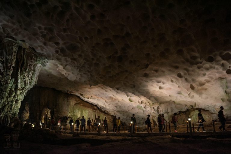 Silhouetted people walking inside illuminated cave.
