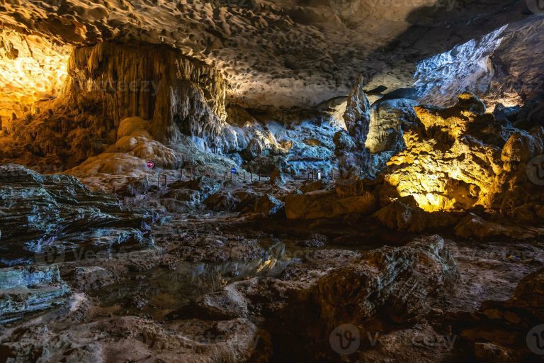 Illuminated stalactites and stalagmites in a colorful cave.